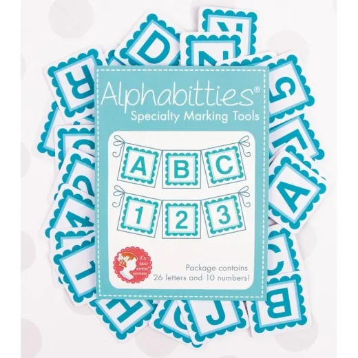 Alphabitties Blue – Verpackung mit Plättchen Verpackung der It's Sew Emma Alphabitties in Blue, umgeben von verstreuten Buchstaben- und Zahlenplättchen