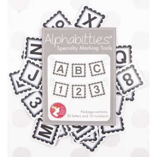 Alphabitties Gray – Verpackung mit Plättchen Verpackung der It's Sew Emma Alphabitties in Gray, umgeben von verstreuten Buchstaben- und Zahlenplättchen