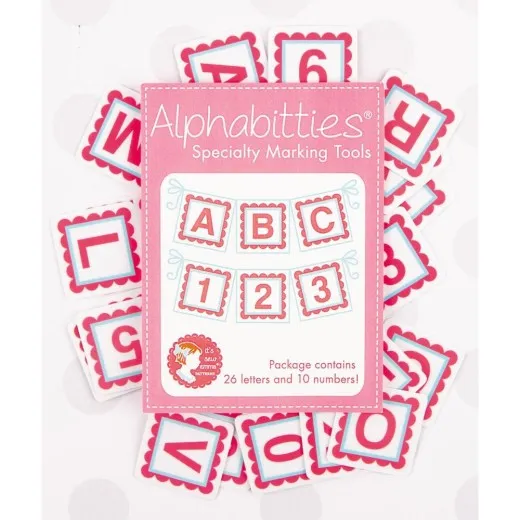 Verpackung der It's Sew Emma Alphabitties in Pink, umgeben von verstreuten Buchstaben- und Zahlenplättchen