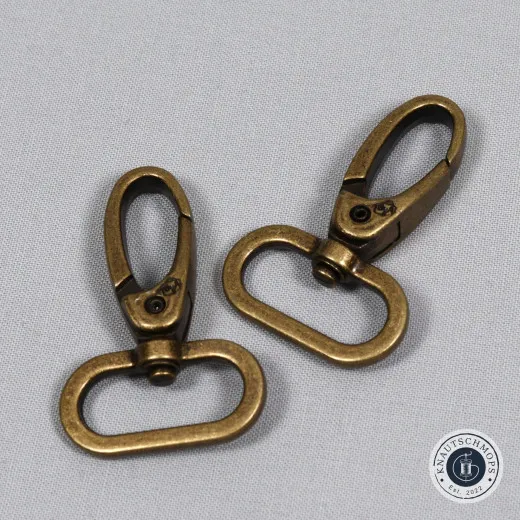 Zwei ByAnnie's Drehkarabinerhaken in Antique Brass auf grauem Stoffuntergrund