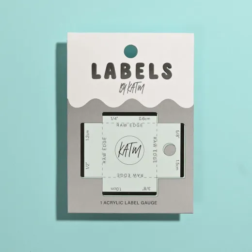 KATM Label Gauge Verpackung Verpackung der KATM Label Gauge Positionier-Schablone in Tea Green auf türkisem Hintergrund