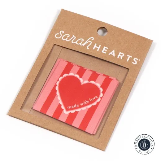 Label auf Verpackungskarte Sarah Hearts großes Weblabel „Made with Love“ mit rotem Herz auf rosa-rot gestreiftem Stoff, auf der Verpackungskarte.