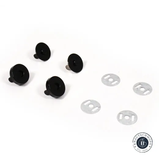 Vier schwarze Magnet-Druckknopf-Kappen und vier passende Metall-Unterlegscheiben lose auf weißem Hintergrund.