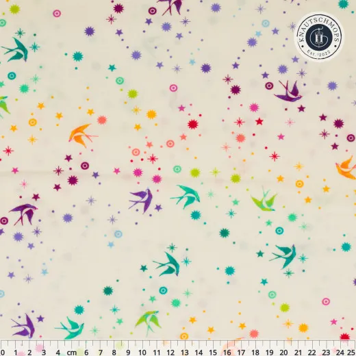 Flach ausgebreiteter Baumwollstoff „Fairy Dust“ in Cotton Candy mit Zentimeter-Maßstab: bunte Schwalben und Sternchen-Konfetti auf Creme.