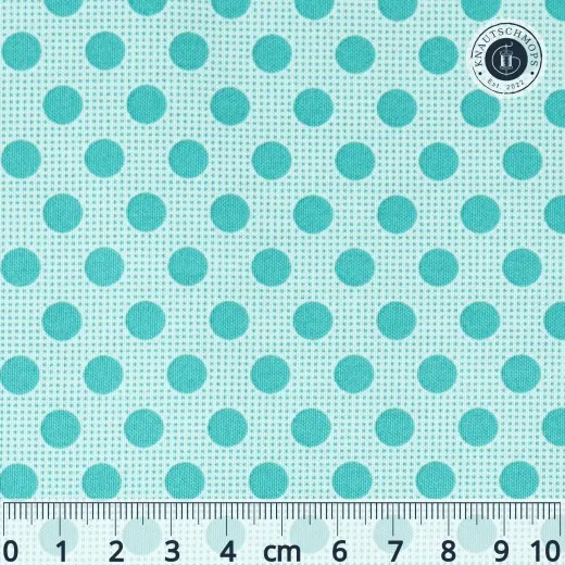 Nahaufnahme des Tilda-Musters „Basic Dots" in Dark Teal mit dunkeltürkisen, ca. 7mm großen Punkten auf mintgrünem Fond, mit Maßband zum Größenvergleich.