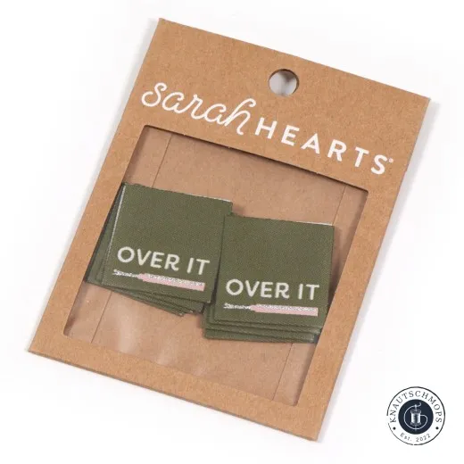 Sarah Hearts Weblabel „Over It“ in Olive mit rosa-silbernem Nahttrenner-Symbol auf der Verpackungskarte.