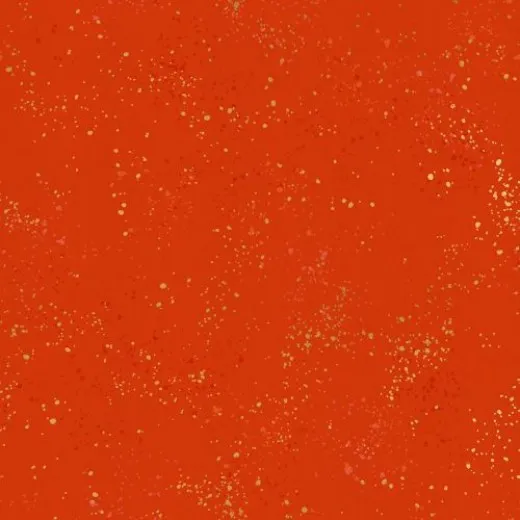Speckled Warm Red – Stoffdetail Nahaufnahme des melierten Baumwollstoffs Speckled in Warm Red mit goldmetallic- und pinkfarbenen Farbspritzern auf orangerotem Grund, mit Maßband am Bildrand.