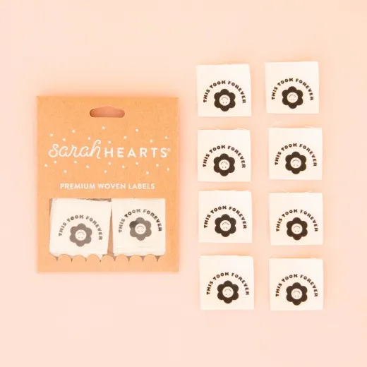 Verpackung der Sarah Hearts Weblabels „This Took Forever" mit Blumen-Smiley-Motiv auf rosa Hintergrund