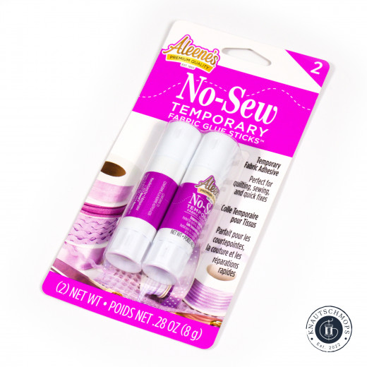 Verpackung – Frontalansicht Verpackung der Aleene's No-Sew Temporary Fabric Glue Sticks, 2er-Set, mit Bandspule im Hintergrund