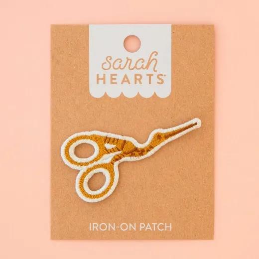 Verpackung Frontalansicht Verpackung des Sarah Hearts Aufnähers „Storchenschere" mit goldbestickter Stickschere in Storchenform.
