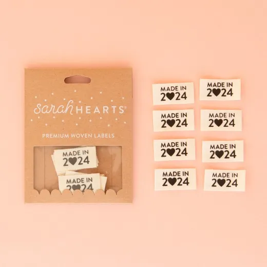 Verpackung der Sarah Hearts Weblabel „Made in 2024" mit acht naturfarbenen Labels und schwarzem Siebdruck-Schriftzug mit Herz statt Null.