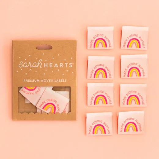 Kraftpapier-Verpackung „Made during Naptime" neben acht rosafarbenen Weblabels mit Regenbogen in Pink, Koralle und Gelb.