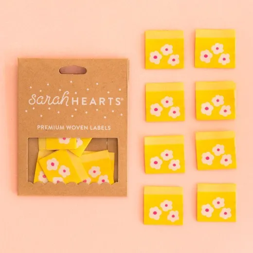 Kraftpapier-Verpackung „Yellow Daisy" neben acht gelben Weblabels mit je drei weißen Gänseblümchen.