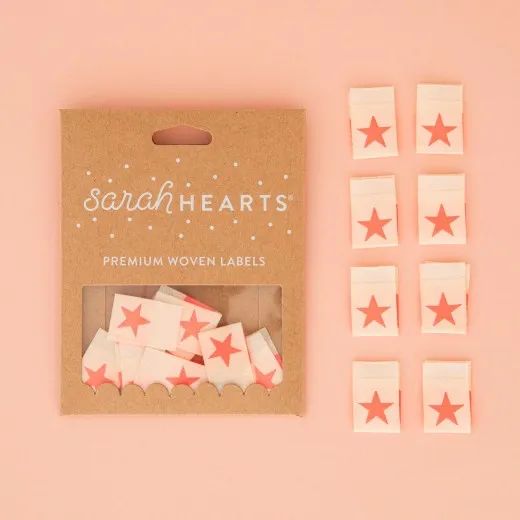 Sarah-Hearts-Verpackung „Star" in Neonpink, daneben alle acht Weblabel aus weichem Polyester.