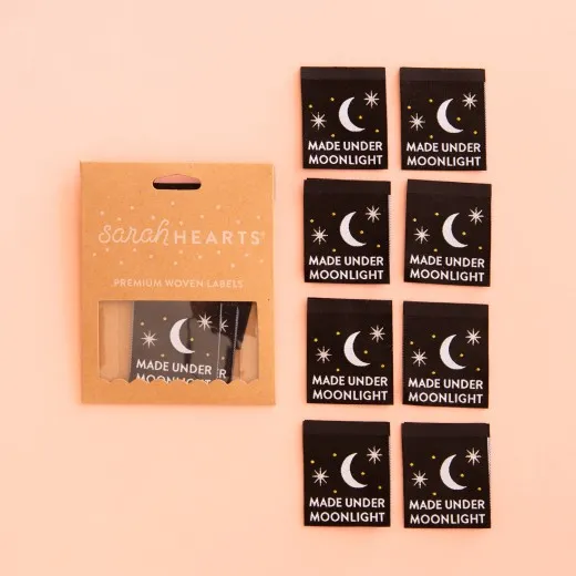 Sarah-Hearts-Weblabel „Made Under Moonlight" in Kraftpapier-Verpackung neben allen acht schwarzen Labels mit Mond- und Sternmotiv.
