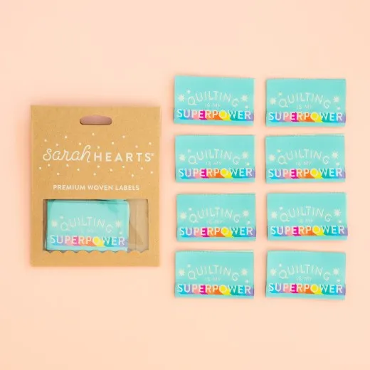 Sarah-Hearts-Weblabel „Quilting is my Superpower" in Kraftpapier-Verpackung neben allen acht mintfarbenen Labels mit Regenbogen-Schriftzug.