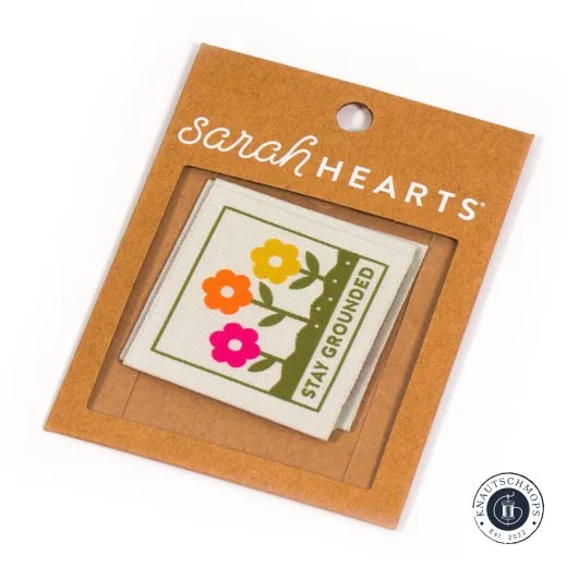 Verpackung mit Weblabels Sarah Hearts Weblabel „Stay Grounded“ mit Blumenmotiv, sichtbar durch das Fenster der Verpackung.