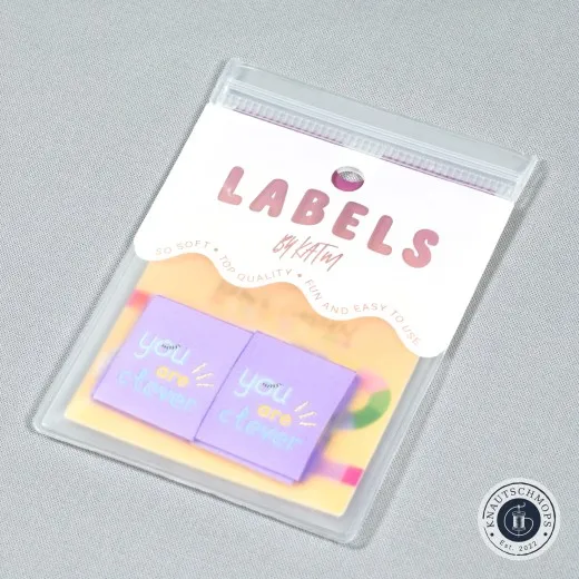„You Are Clever"-Labels in Flieder aus der Kollaboration mit Brook Gossen, sichtbar in der Original-Verpackungskarte, schräg fotografiert.