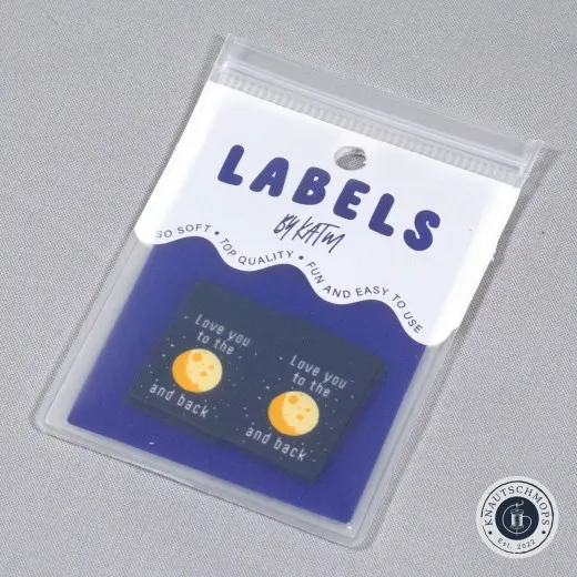 Verpackung schräg fotografiert Zwei „Love You To The Moon and Back"-Labels mit Mond-Motiv auf Sternenhimmel, sichtbar in der Original-Verpackungskarte „Labels by KATM".