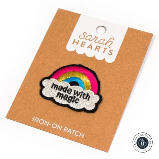 Sarah Hearts Iron-On Patch „Made with Magic" mit buntem Regenbogen und Wolke, schräg auf der Verpackungskarte fotografiert.