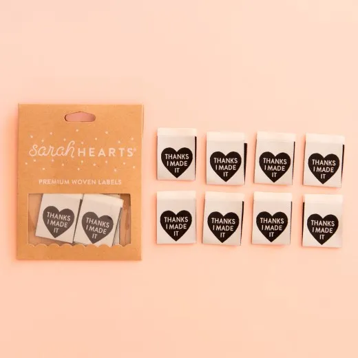 Verpackung Thanks I Made It Sarah Hearts Verpackungskarton mit 8 grauen Weblabels, schwarzes Herz mit Schriftzug „Thanks I Made It" auf rosa Hintergrund.