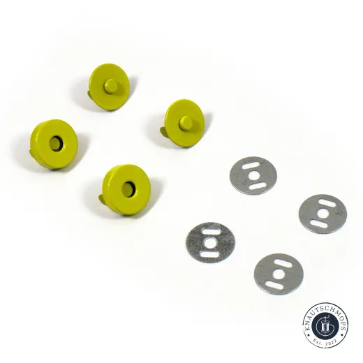 Vier gelbgrüne Magnet-Druckknopf-Hälften und vier ovale Metall-Unterlegscheiben locker auf weißem Untergrund verteilt.
