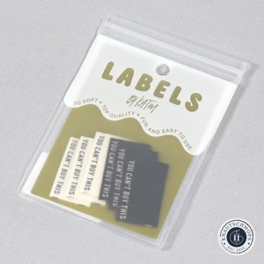 Verpackung der KATM-Labels You Can't Buy This in Schwarz/Creme, Ansicht schräg von oben mit sichtbaren Stoffetiketten
