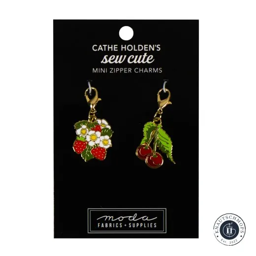 Zwei goldene Emaille-Anhänger von Cathe Holden: Erdbeeren mit Blüten und Kirschen mit Blatt, auf Verpackungskarte 'Mini Zipper Charms', Frontalansicht.