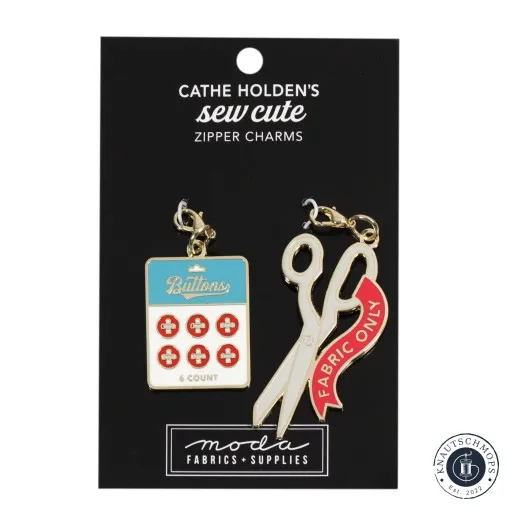 Zwei goldene Emaille-Anhänger von Cathe Holden: eine Schere und eine Knopf-Karte, auf Verpackungskarte, schräge Ansicht.