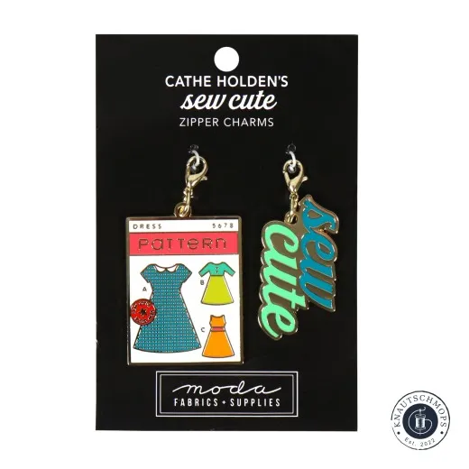 Zwei goldene Emaille-Anhänger von Cathe Holden: eine Kleider-Schnittmusterpackung und der Schriftzug 'sew cute', auf Verpackungskarte.