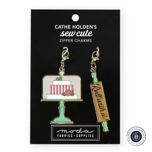 Zipper Charms Torte & Nudelholz Zwei goldene Emaille-Anhänger von Cathe Holden: eine mehrstöckige Torte auf Etagere und ein Nudelholz mit Schriftzug 'Roll with it!', auf Verpackungskarte.