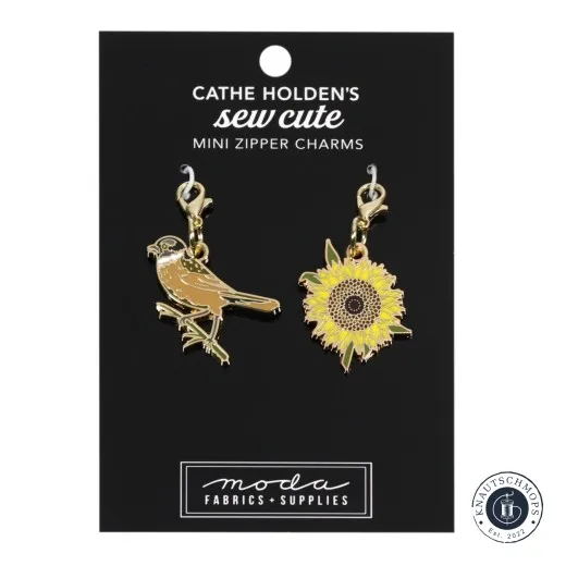 Zwei goldene Emaille-Anhänger von Cathe Holden: ein Vogel und eine Sonnenblume, auf Verpackungskarte.