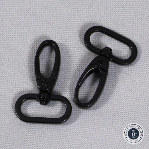 Zwei Karabinerhaken freigestellt Zwei schwarze, drehbare 1-Zoll-Karabinerhaken von ByAnnie's auf grauem Stoffuntergrund.