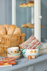Gefaltete Tilda-Blenderstoffe der Kollektion Village Life in einer Keramikschale, dekoriert neben einem Brotkorb und Garnrollen.