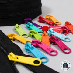 Nahaufnahme mehrerer bunter XL-Zipper neben dem schwarzen Reißverschlussband