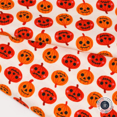 Nahaufnahme des Kürbis-Stoffs mit gefalteter Stoffkante, orange-rote Jack-O-Lantern-Gesichter auf Creme