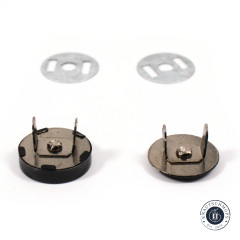 Zwei Metall-Unterlegscheiben und zwei schwarze Druckknopf-Rückseiten mit sichtbaren Metallzapfen zur Befestigung im Stoff.