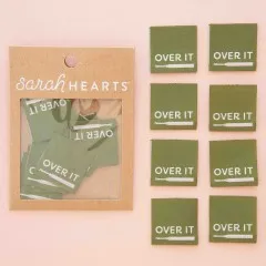 Acht „Over It“-Labels mit Nahttrenner-Symbol ausgelegt auf rosa Hintergrund.
