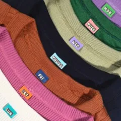 Alle sieben Wochentag-Label eingenäht in die Kragen einer bunten Kleidungsstück-Reihe.