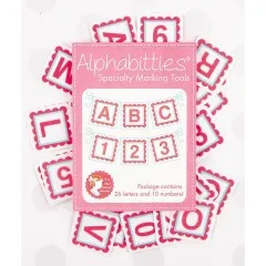 Verpackung der It's Sew Emma Alphabitties in Pink, umgeben von verstreuten Buchstaben- und Zahlenplättchen