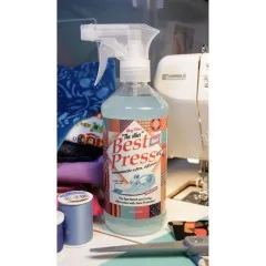 Die Best-Press-Flasche auf einem Nähtisch zwischen Stoffen, Garnrollen und einer Nähmaschine.