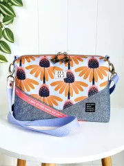 Umhängetasche von INIMI Bags aus dem Echinacea-Stoff kombiniert mit graublauem Jeansstoff, fotografiert vor weißer Wand mit Grünpflanze.