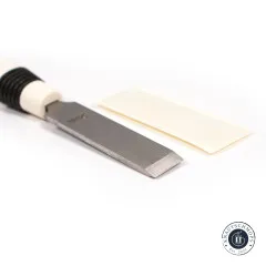 Der Knopflochaufschneider mit Kunststoffgriff neben dem beiliegenden Schutzblock aus Holz.