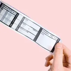 Ein Stück des Fabric ID Tape mit Feldern für Fasergehalt, Breite, Länge und Herkunft, ausgerollt und in der Hand gehalten vor rosa Hintergrund.