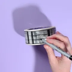 Hand beschriftet ein Feld der Fabric-ID-Tape-Rolle mit einem Permanentmarker vor violettem Hintergrund.