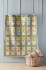 Patchwork-Quilt mit Blumentopf-Muster aus der Spring-Kollektion, an der Wand aufgehängt, mit Kissenkorb davor.