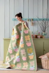 Frau präsentiert den aufgeschlagenen Patchwork-Quilt mit Blumentopf-Muster aus der Spring-Kollektion.