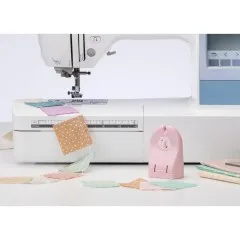 Der Clover „Quick Cut" Fadenschneider steht griffbereit neben einer Nähmaschine mit Patchwork-Reststücken.