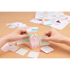 Zwei Hände trennen mit dem Clover „Quick Cut" Fadenschneider eine Quiltkette aus zusammengenähten Stoffquadraten.
