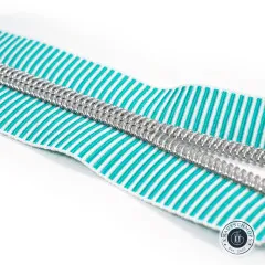 Diagonale Nahaufnahme der silberfarbenen Zähne auf dem türkis-weiß gestreiften Zipper-Band vor weißem Hintergrund.
